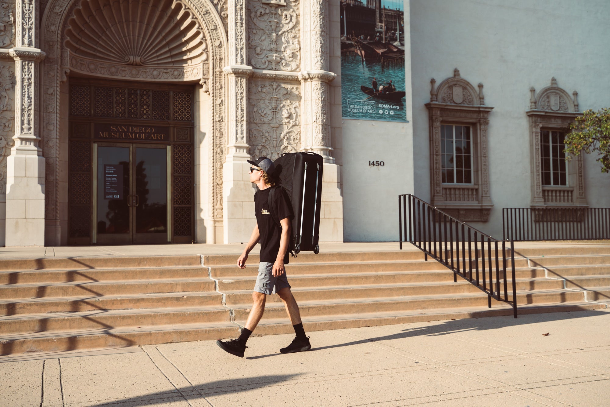 A young man walking in front of the San Diego Museum of Art in Balboa Park, while carrying the B2 bicycle travel case on his back. 